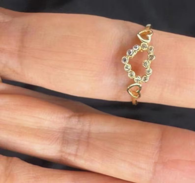 Gold ring with heart designs on a person's finger against a black background