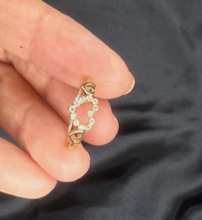 Gold ring with small stones held between fingers against a dark background