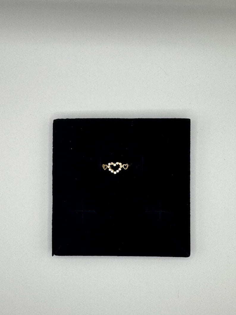 Gold heart-shaped earring on a black square pad against a light gray background